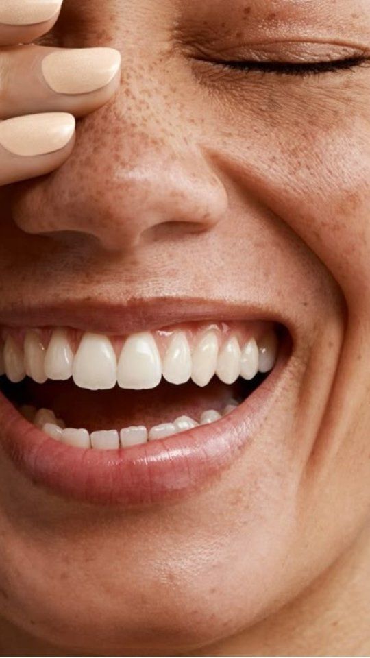 Close-up of smiling woman with healthy white teeth touching cheek.