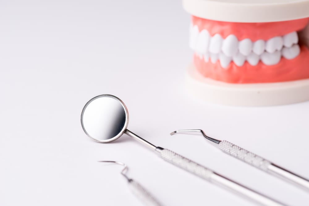 Dental tools on white surface, dentures in background