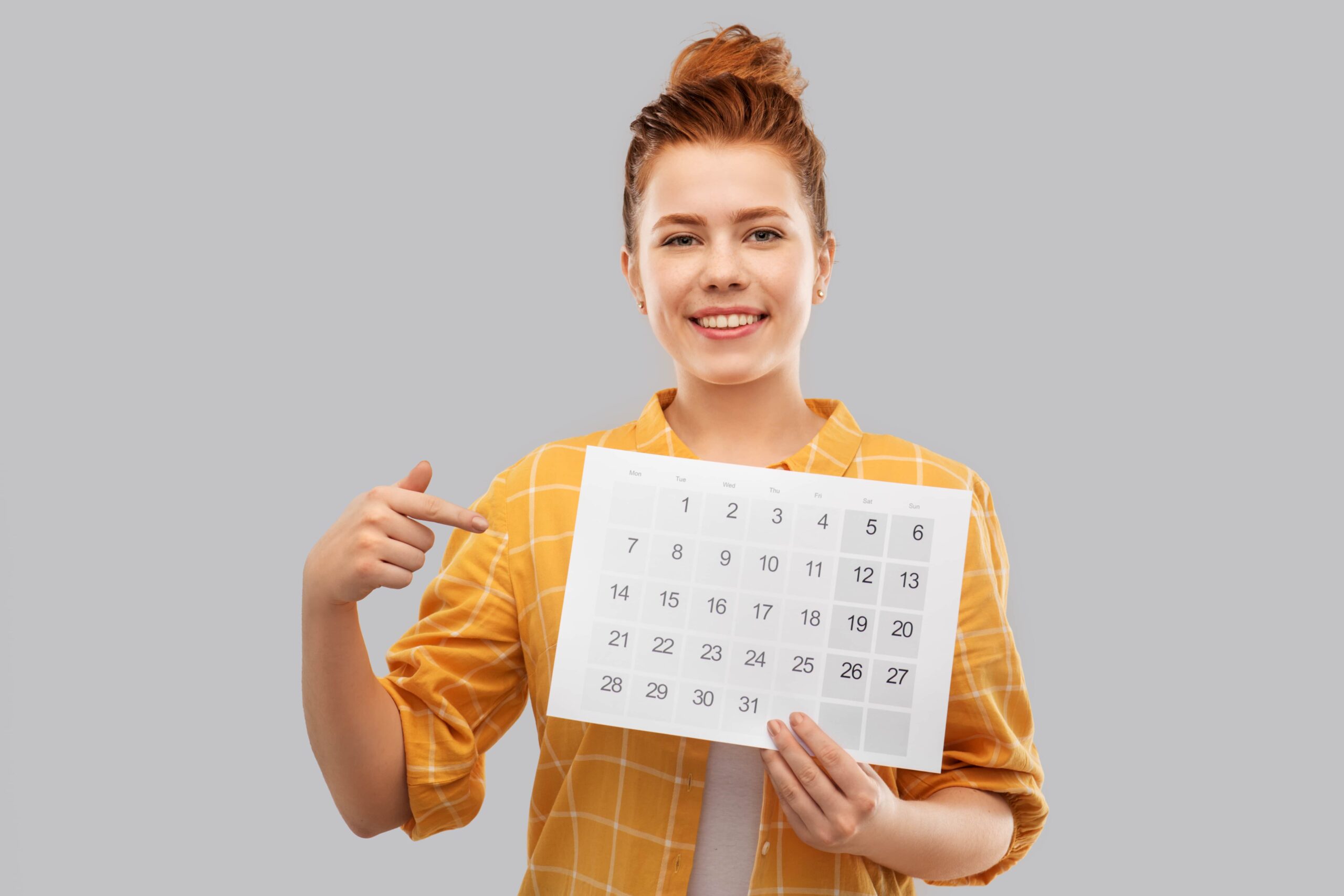 Smiling young woman holding and pointing at calendar
