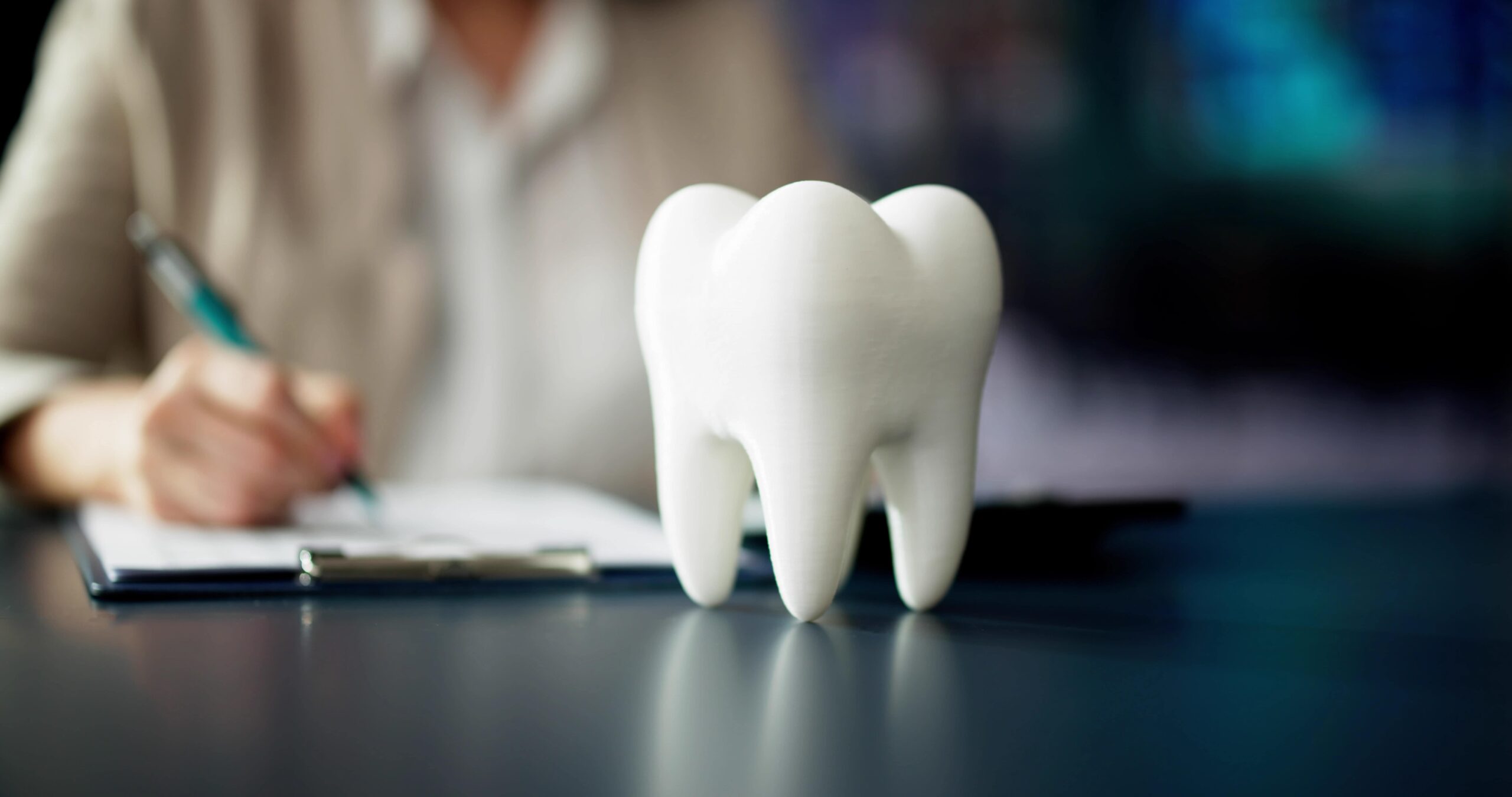 Tooth replica on desk, person in background looking at papers